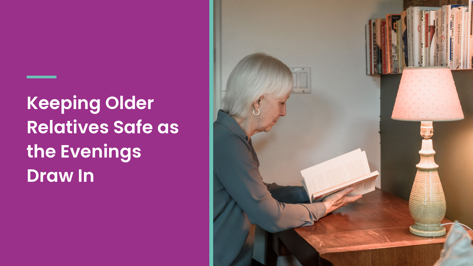 An older woman with white hair reads a book at a wooden desk beside a softly glowing table lamp at home.